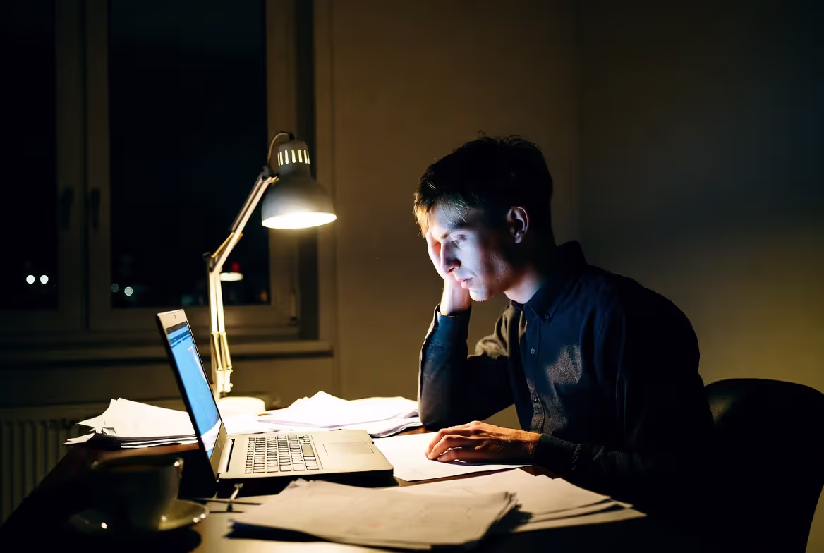 Tired person working late at night surrounded by documents and laptop