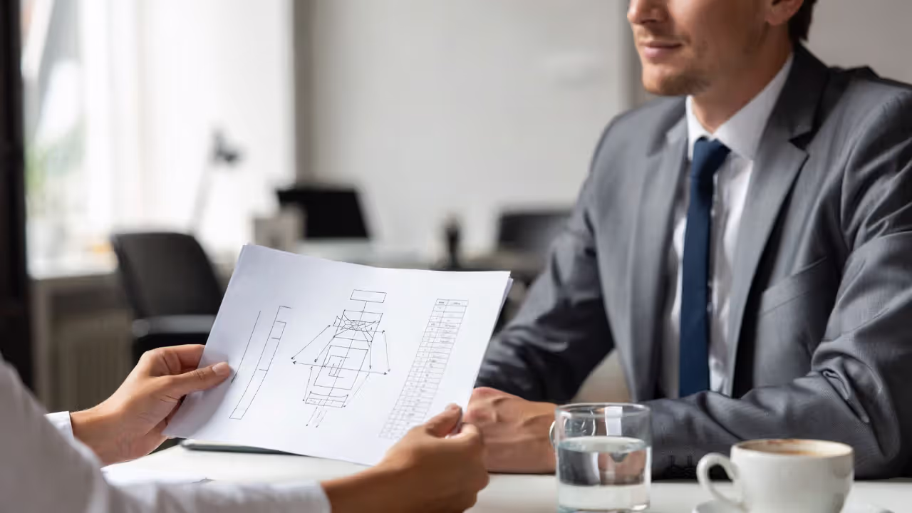 One-on-one feedback conversation with a document being reviewed in a neutral office.